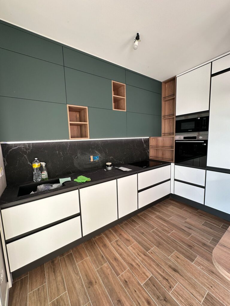 La stessa cucina montata: pensili verdi fino al soffitto con nicchie in legno, schienale in marmo nero, basi bianche
