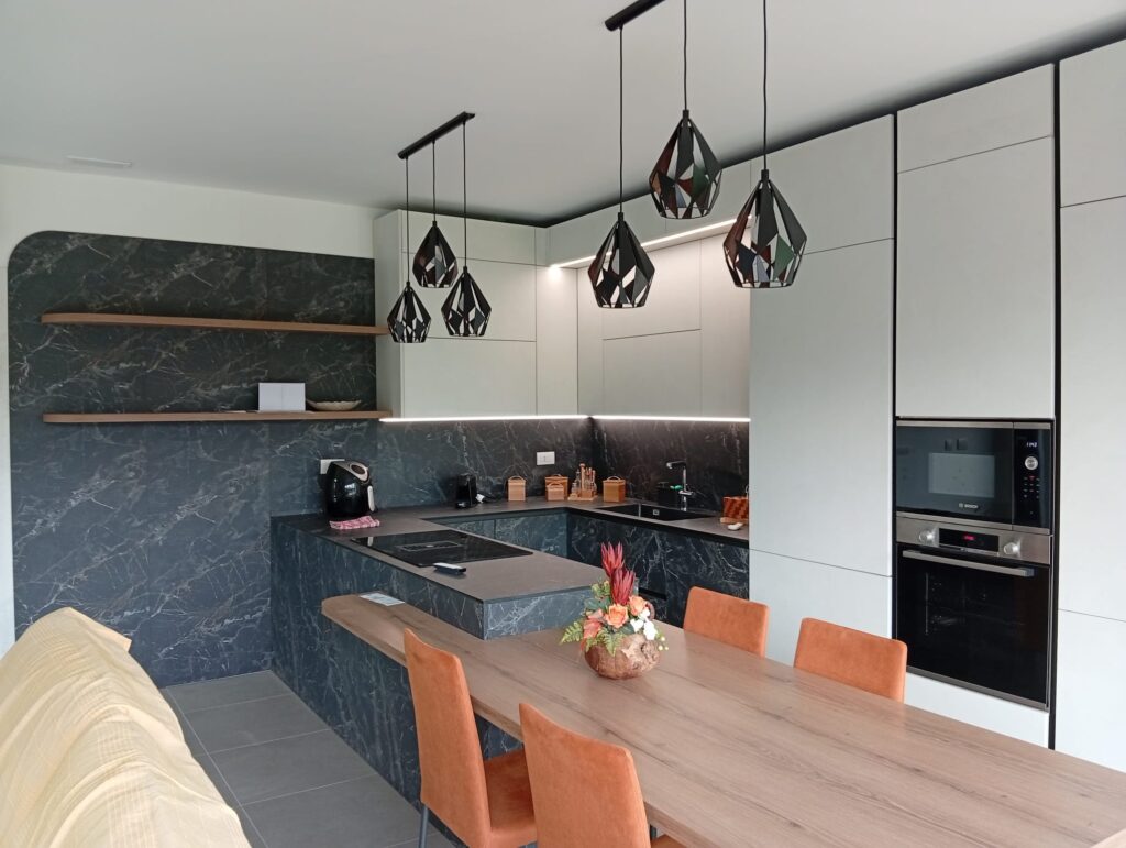Cucina su misura con penisola in legno, top e schienale effetto marmo scuro e colonne bianche
